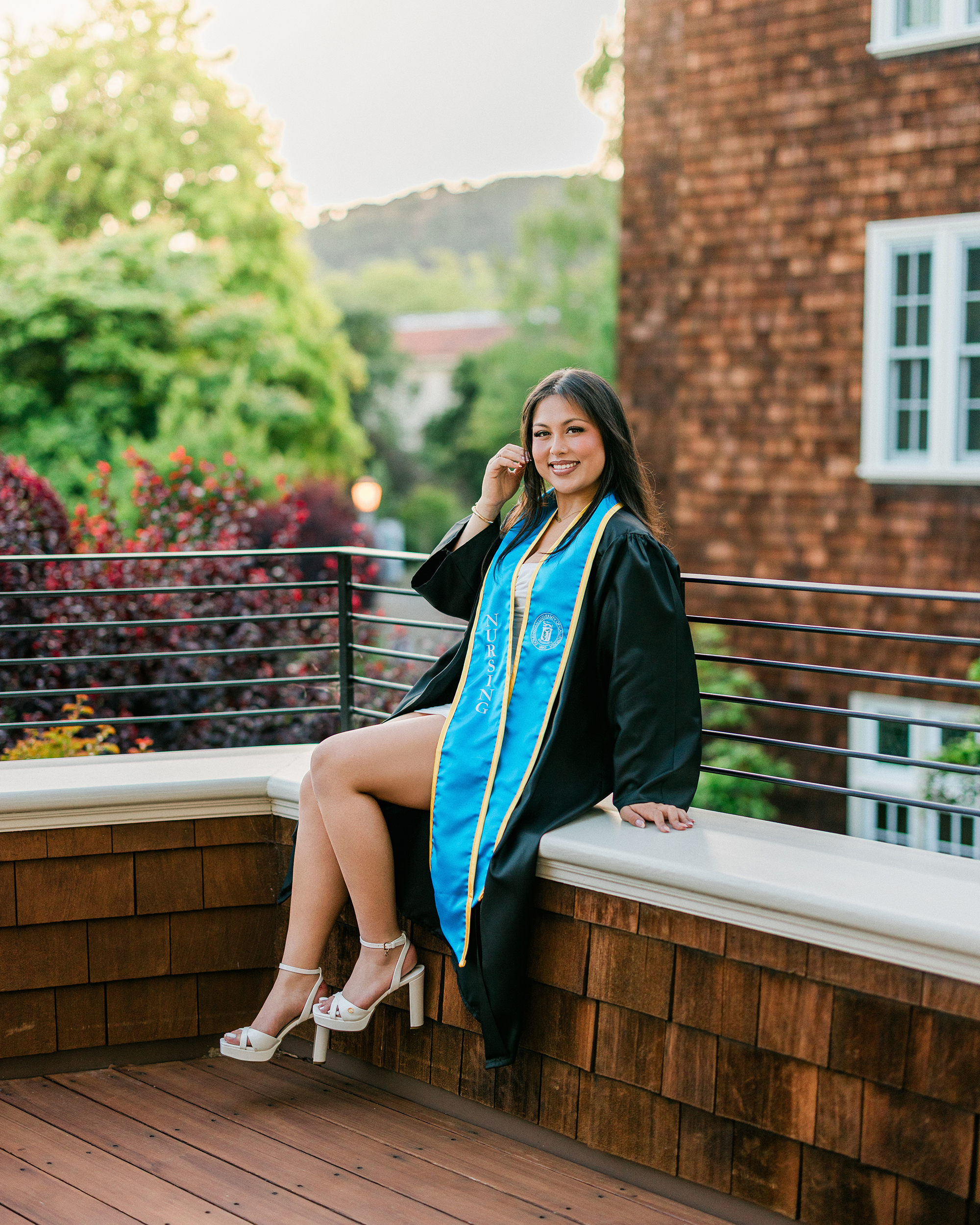 Dominican University nursing graduate sitting on brick ledge during graduation photo session