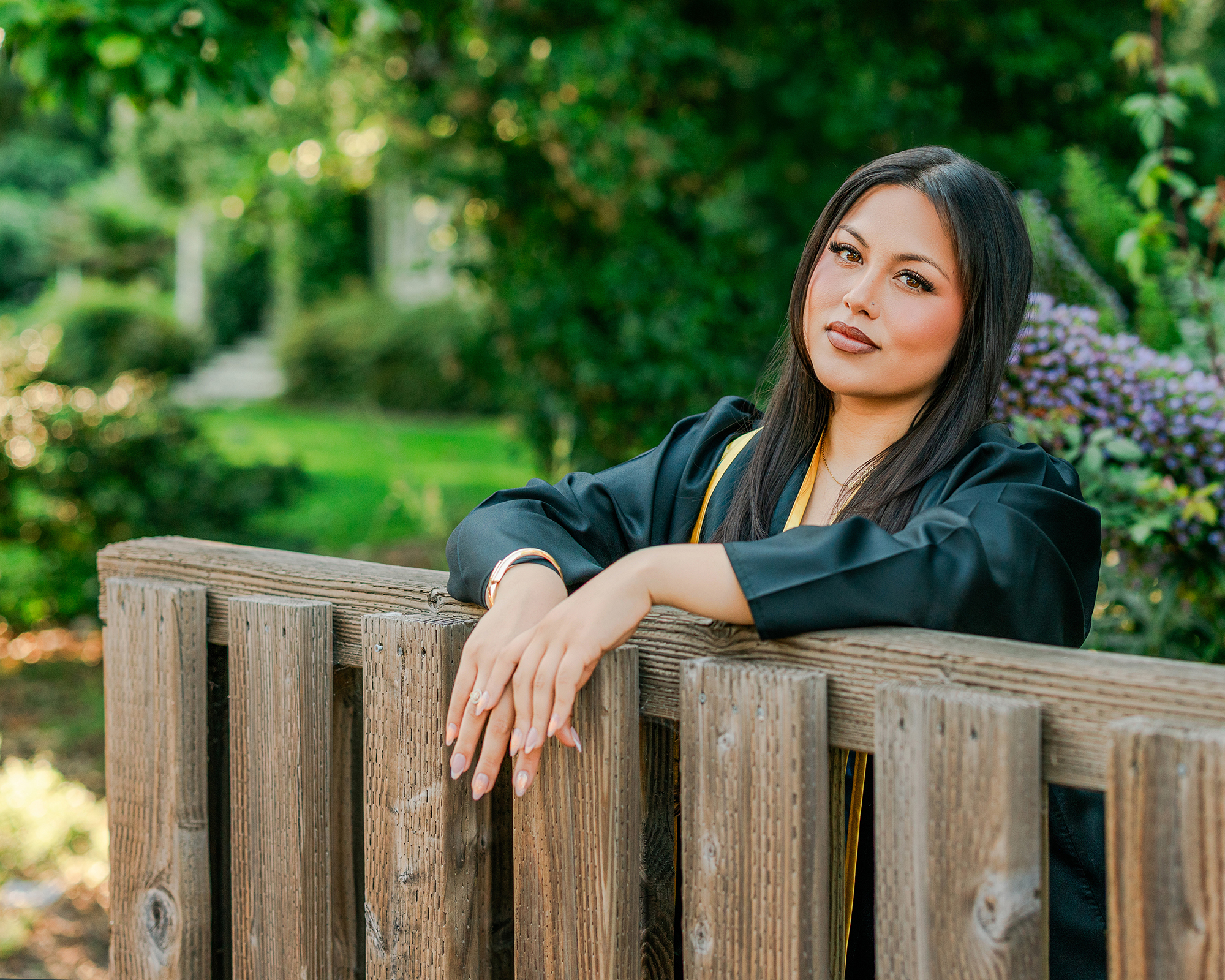 Dominican University nursing graduate leaning on wooden fence during commencement portraits