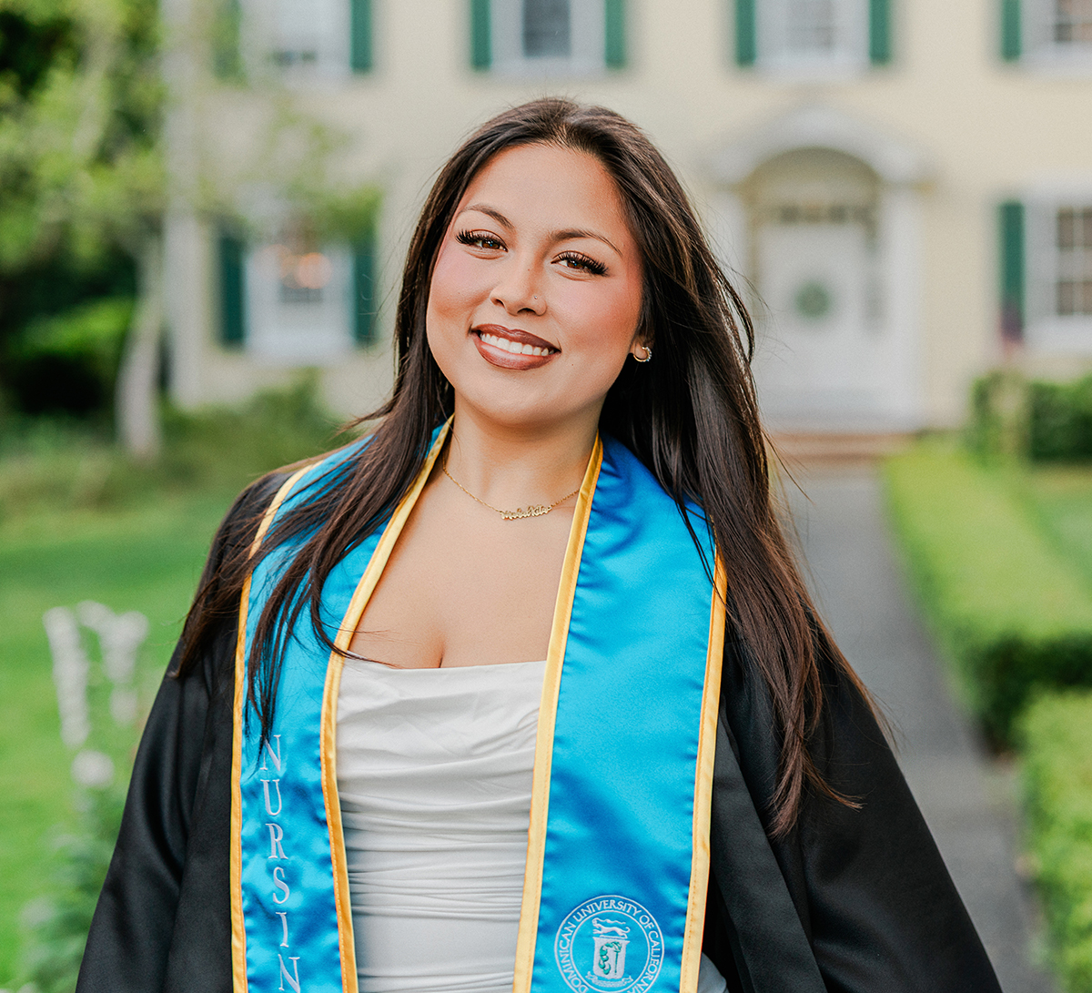 Dominican University nursing graduate smiling in front of historic campus building during graduation portrait session in San Rafael California