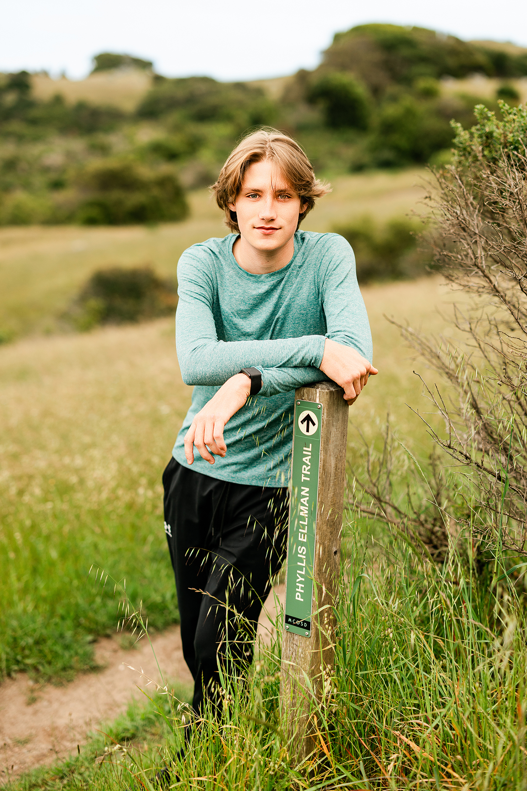 Redwood High School senior leaning on a trail marker along a Marin County hiking and biking trail