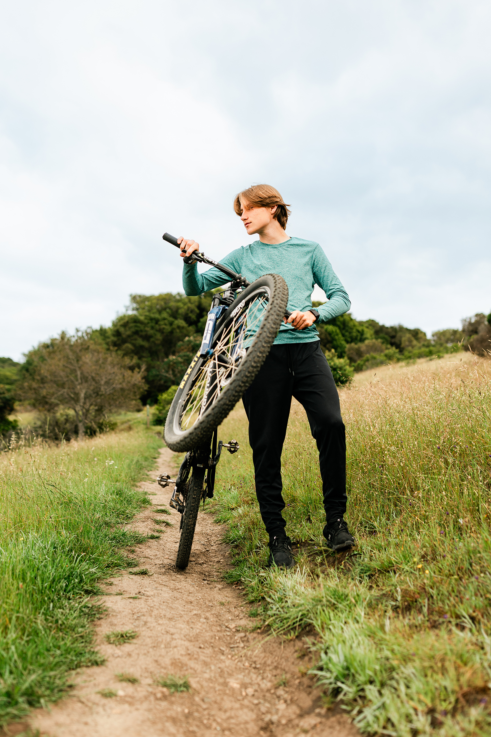 Redwood High School senior mountain biker posing with his bike on a scenic Marin County trail during a senior portrait session