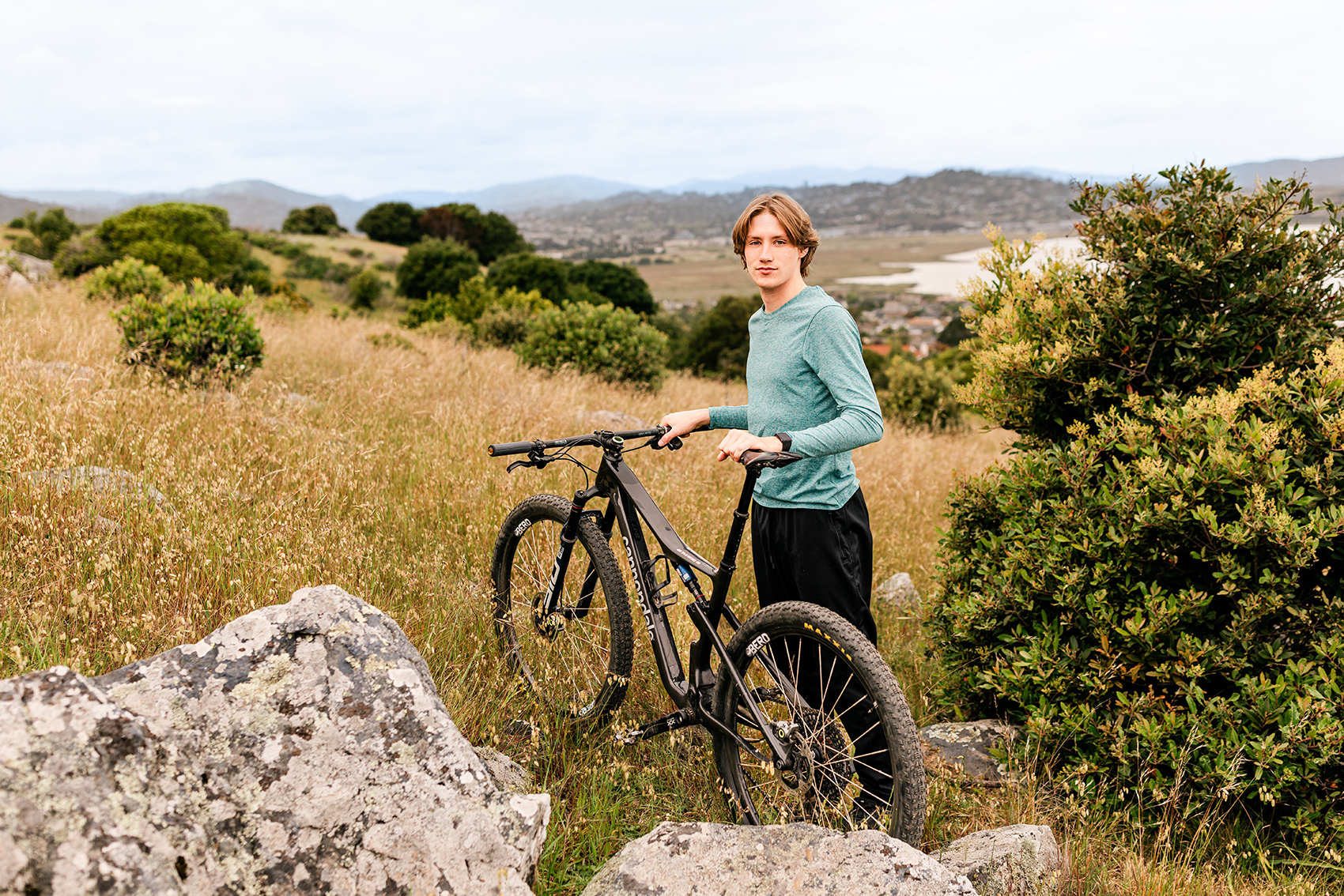 Redwood High School senior mountain biker standing with his bike on a hillside overlooking Marin County and the bay