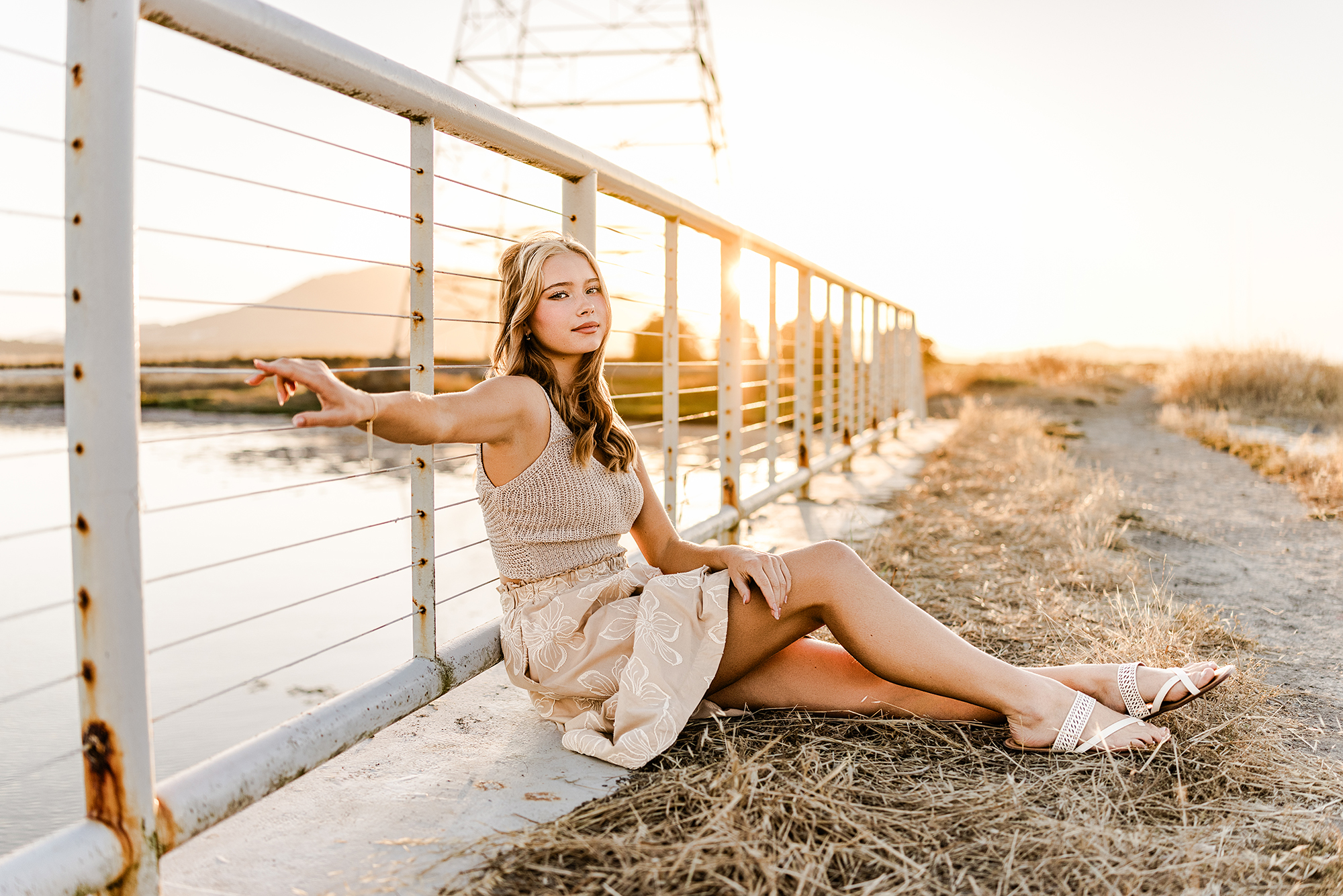 Rising senior Sofia seated beside a bridge overlooking the Marin waterfront during her senior portrait session at sunset.